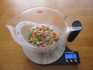 Photograph of Fruity Pebbles in a large measuring cup on a scale.